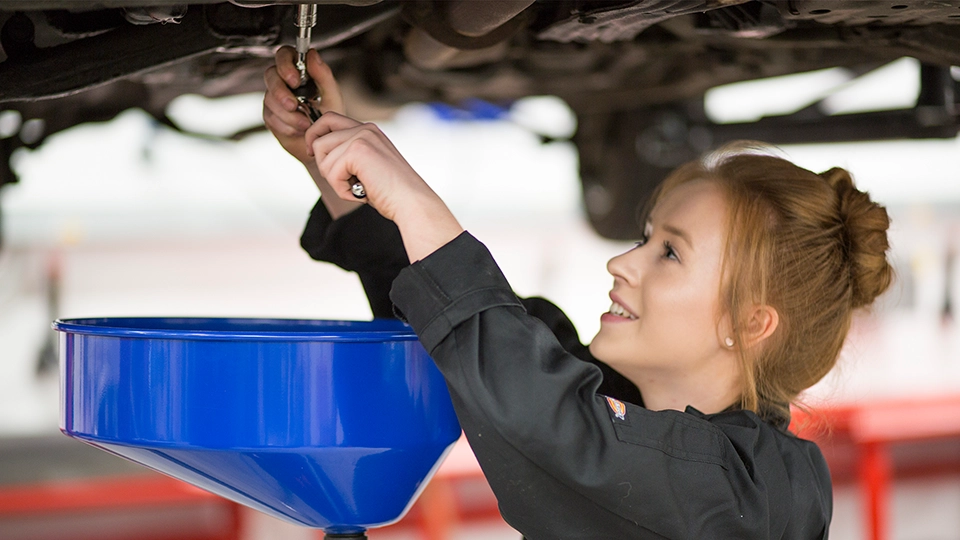 Person using a ratchet above a vehicle with a blue oil drain container positioned below.