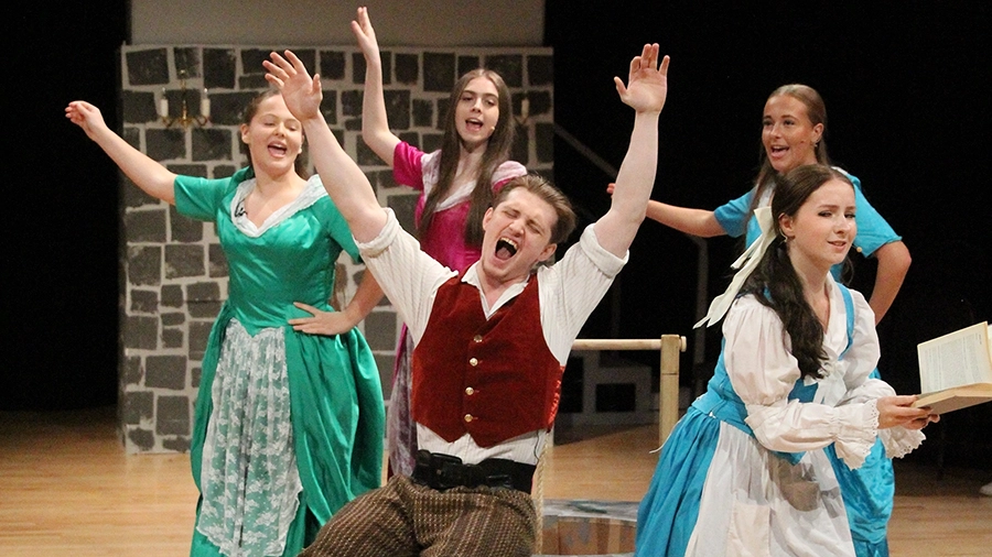 Performers in period costume sing and gesture together on a theatre stage.