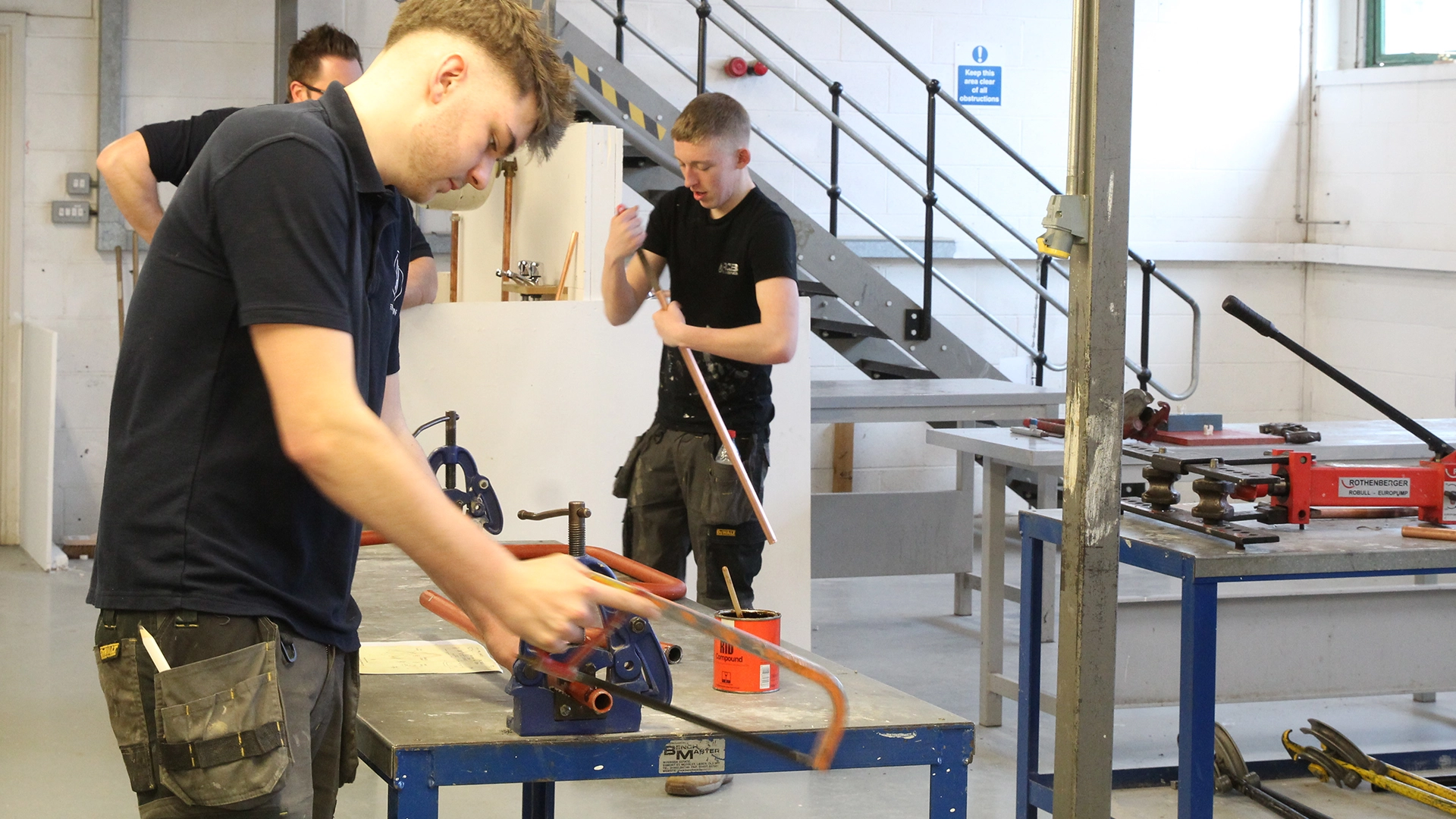 Apprentices cutting and shaping copper pipes at workbenches in a plumbing workshop