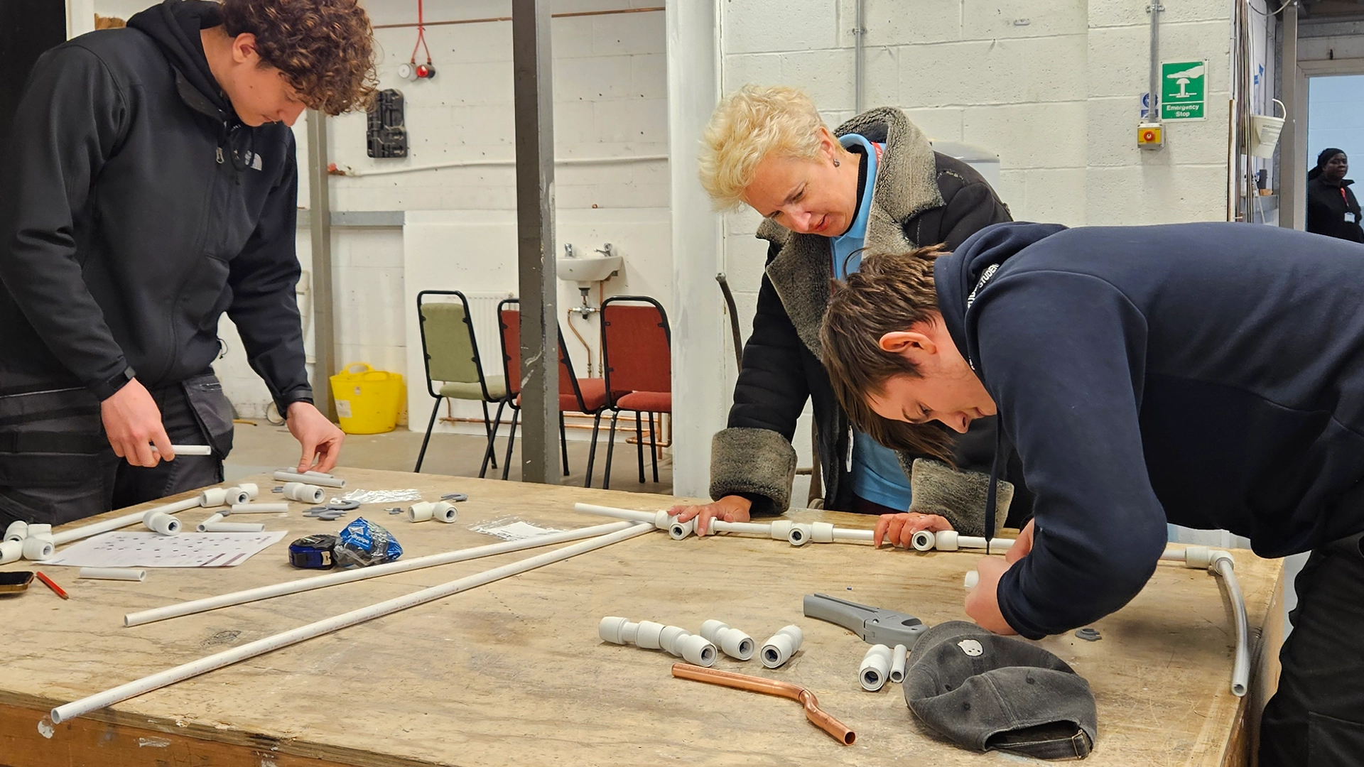 Learners and tutor assembling plastic pipe fittings on a workbench in a workshop