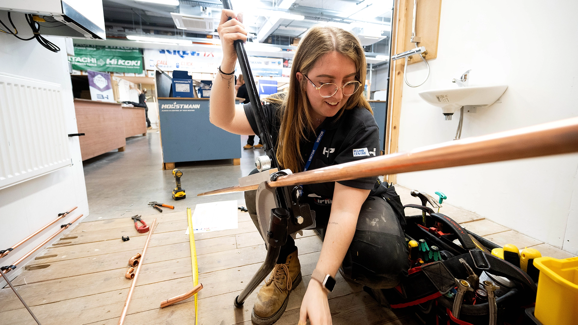 Apprentice bending a copper pipe using a pipe bender on a workshop floor
