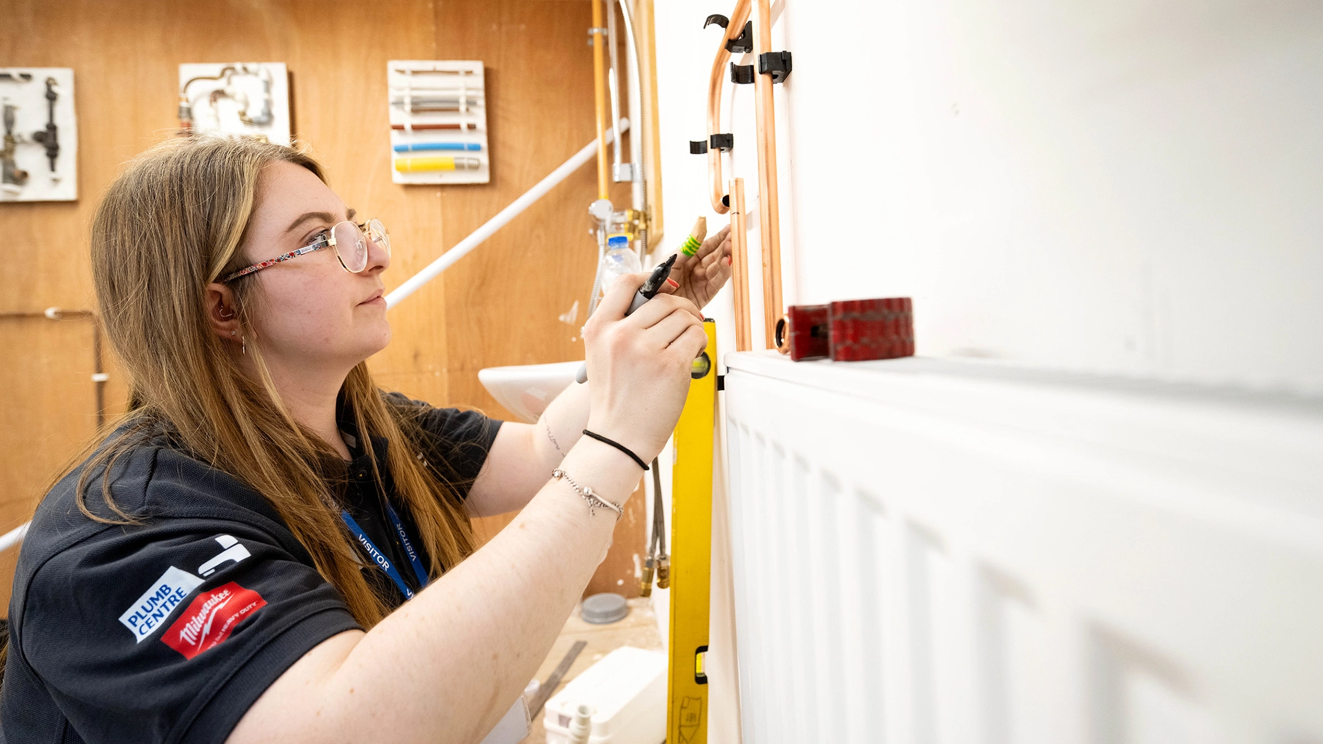 Apprentice measuring and installing copper pipework on a training wall