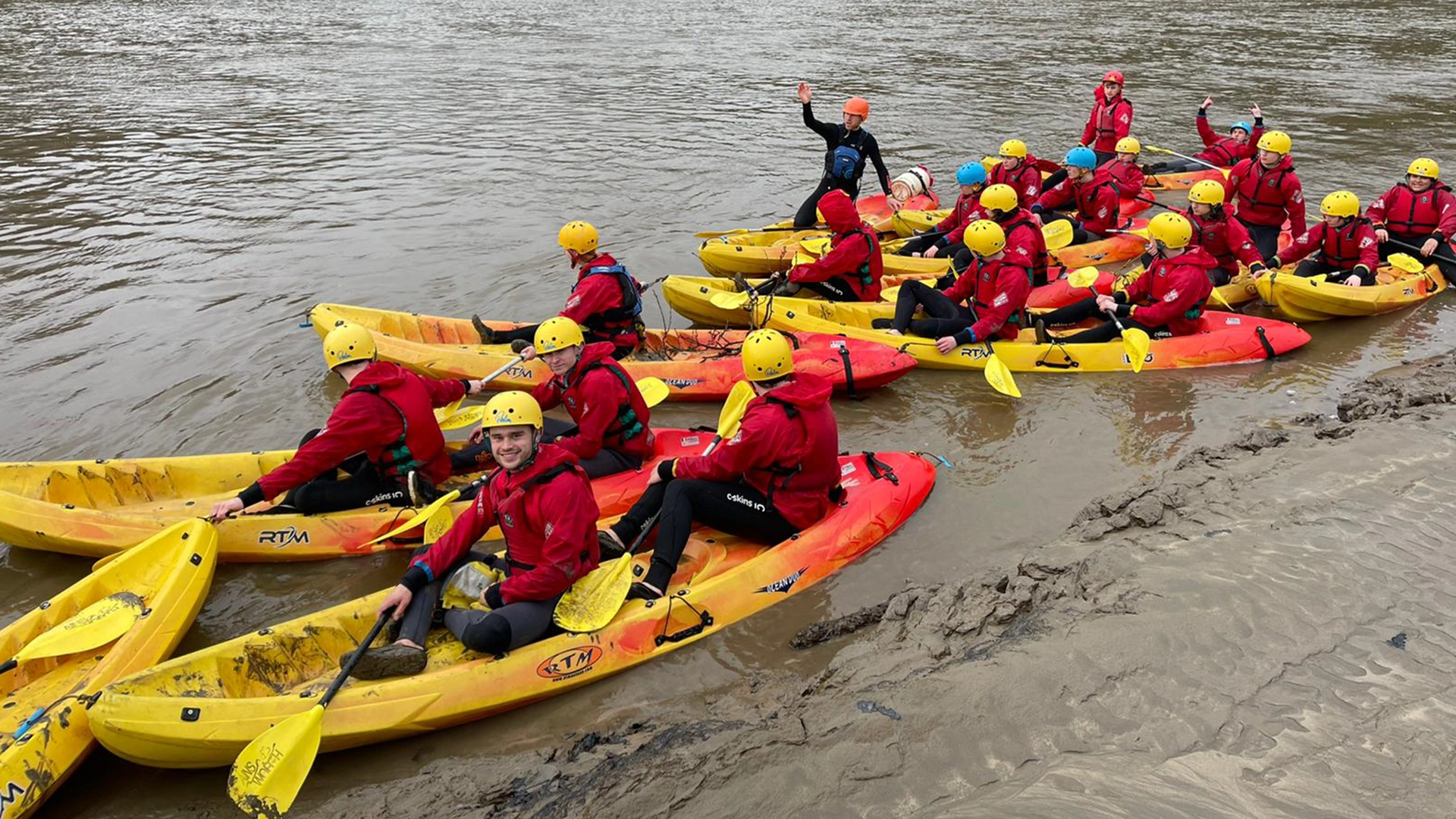 Group of people in helmets kayaking on a river near the shoreline.