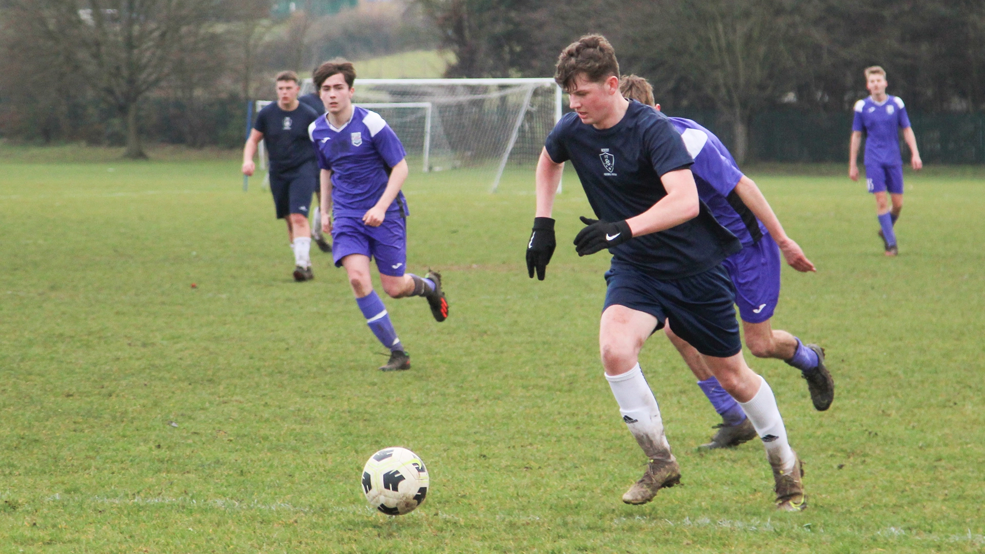 Players running after a football during a match on a grass pitch.