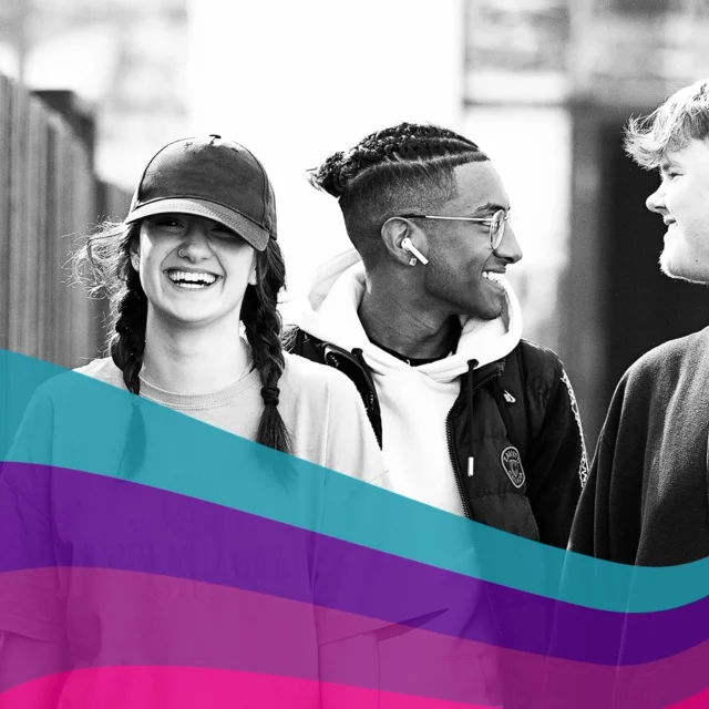 Three students walking outdoors along a fence, talking together, with a coloured graphic overlay at the bottom.