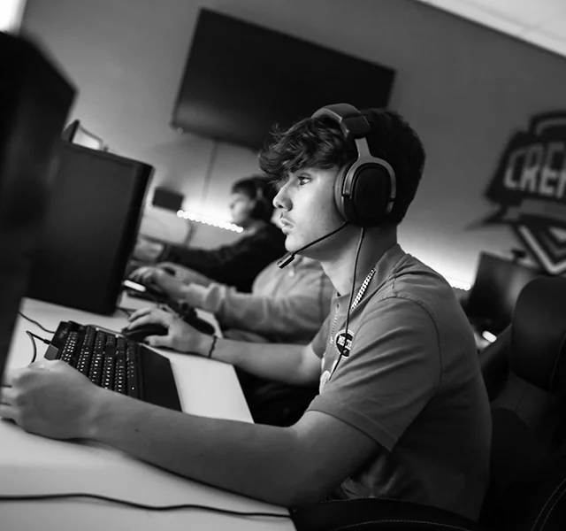 A close-up side view of a person wearing a headset and sitting at a desktop computer in a gaming or esports setup.