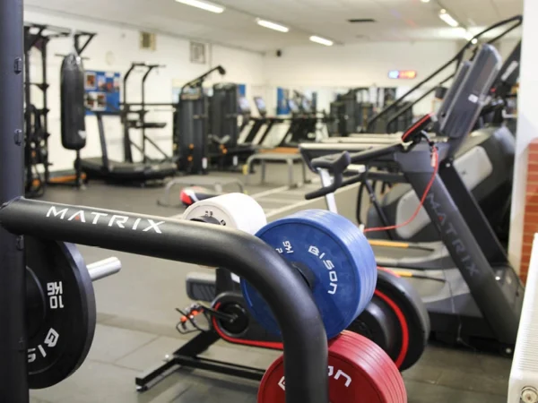 gym space with weight plates on a rack in the foreground and cardio machines and fitness equipment arranged in the background.