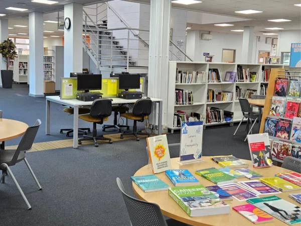 Nescot library with computers, bookcases and study tables, including a display of careers and study skills books in the foreground.