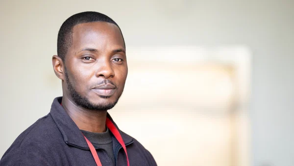 Head-and-shoulders portrait of Security Lead Aaron, wearing a dark zip-up fleece and a red lanyard, facing the camera against a softly blurred indoor background with neutral tones.