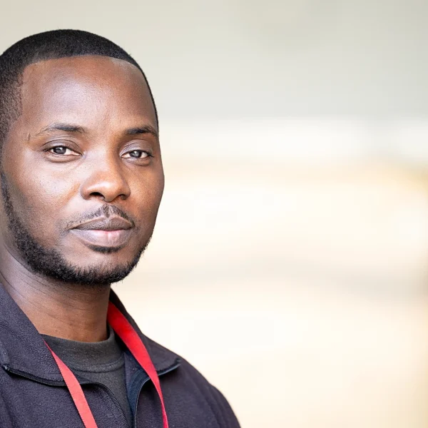 Head-and-shoulders portrait of Security Lead Aaron, wearing a dark zip-up fleece and a red lanyard, facing the camera against a softly blurred indoor background with neutral tones.