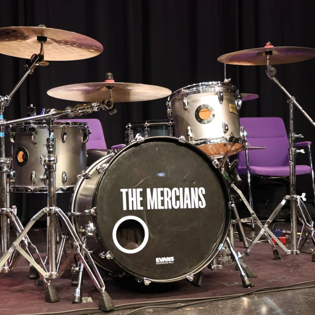 Photo of a drum kit on a stage with 'The Mercians' band name logo on the main drum.
