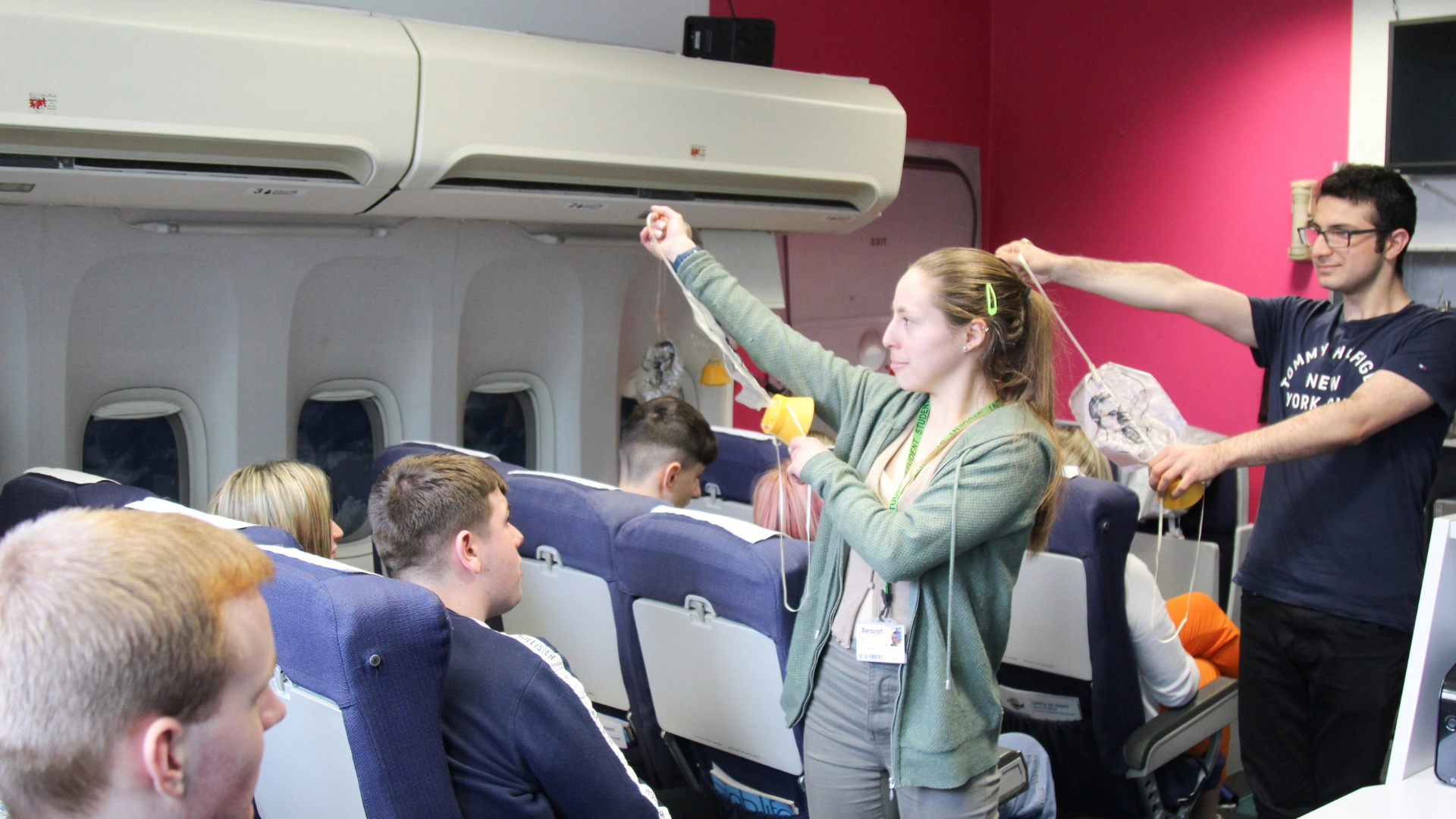 Cabin Room full of passengers with two students demonstrating the use of the oxygen masks.
