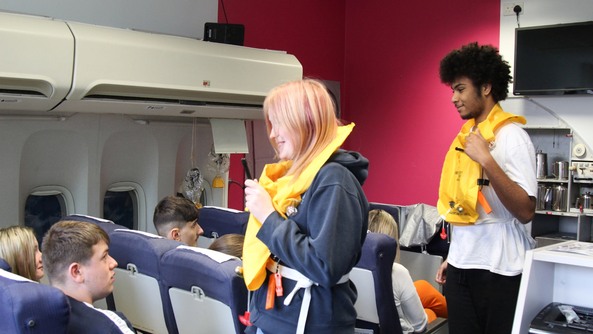 Students demonstrating the use of life jackets to passengers in cabin room.
