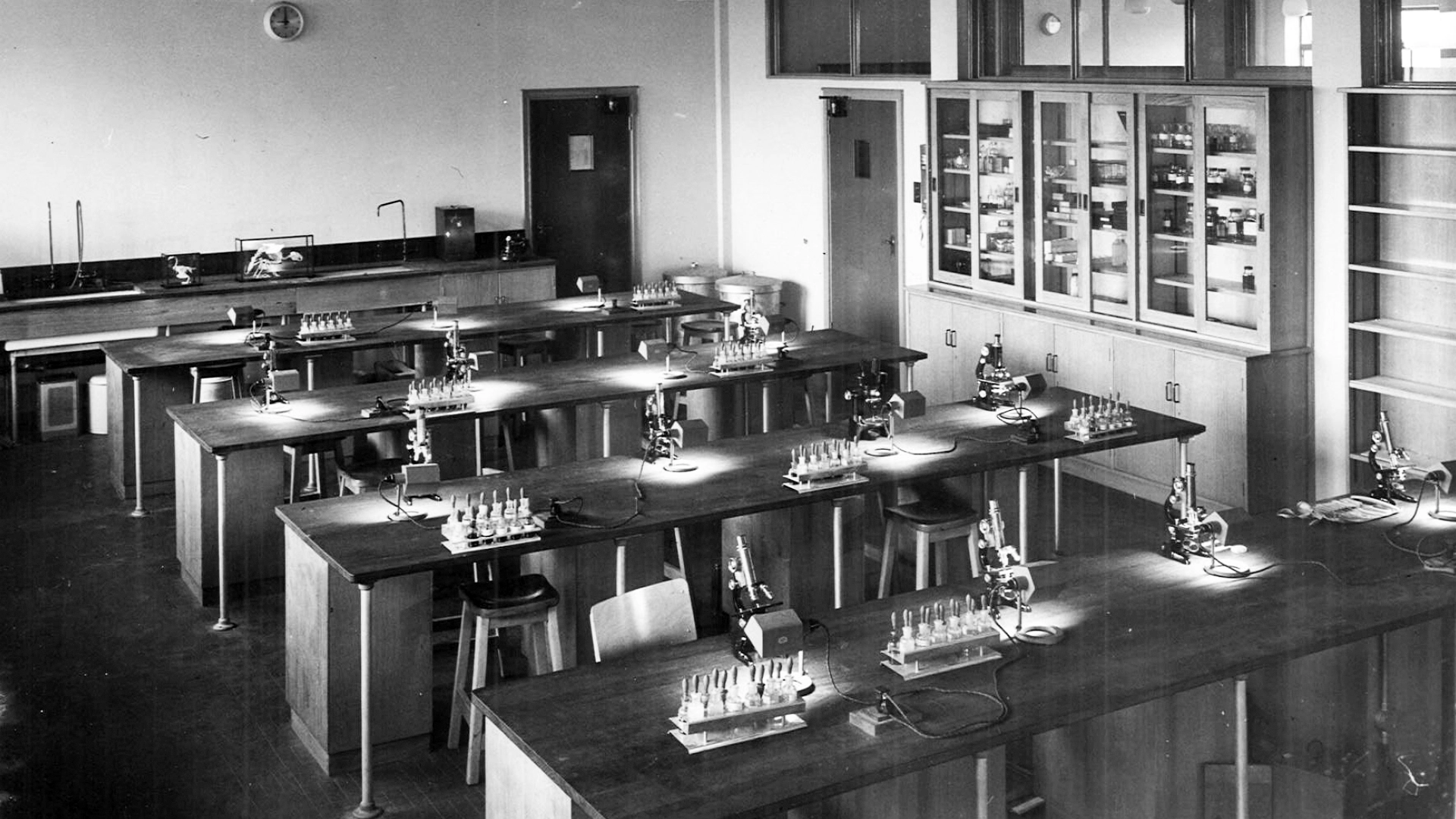 Historic black and white photo showing a laboratory with wooden benches, microscopes and test tubes.
