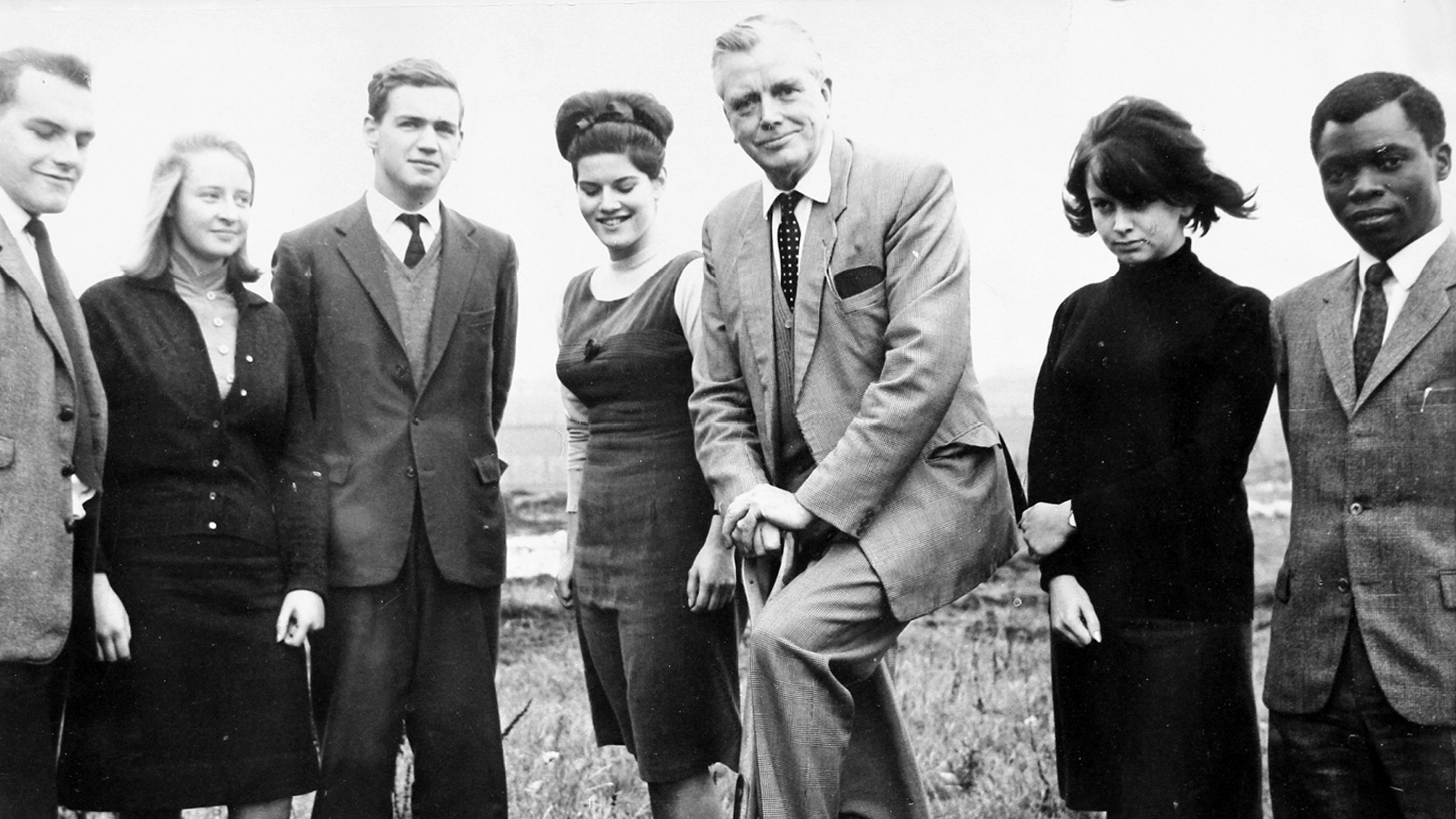 Historic black and white photo of Ewell County Technical College showing staff gathered around the principal who is using a shovel to break ground on the new wing
